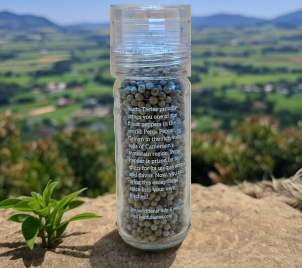Glass jar of Bantu Tastes Penja Pepper with a scenic aerial view of Penja Valley farmland and mountains, highlighting the authentic origin of this premium Cameroon white peppercorn.